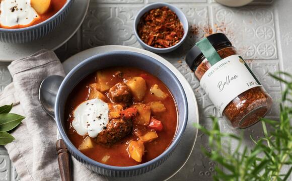 Eine Schale mit Gulasch, daneben ein Glas mit Balkan-Gewürz