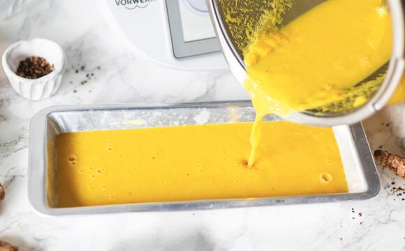 Jemand gießt Kürbissuppe aus dem Mixtopf des Thermomix® in eine flache Form