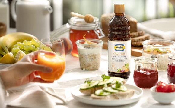 Frühstückstisch mit Obst und Gemüse, ein Glas Saft, eine Flasche LaVita