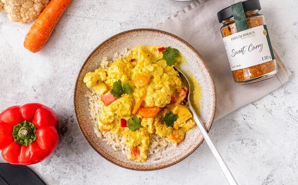 Sweet Curry Gewürz in einem Glas neben einem Teller mit einem Curry-Gericht