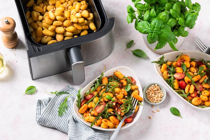 Zwei Schalen mit Gnocchi, Ruccola, Tomaten, von oben fotografiert, daneben der Airfryer
