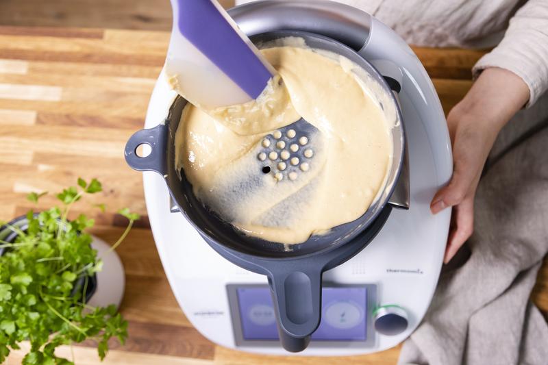 Mit einem Spatel wird Spätzle-Teig durch den WunderSpatzl geschabt.