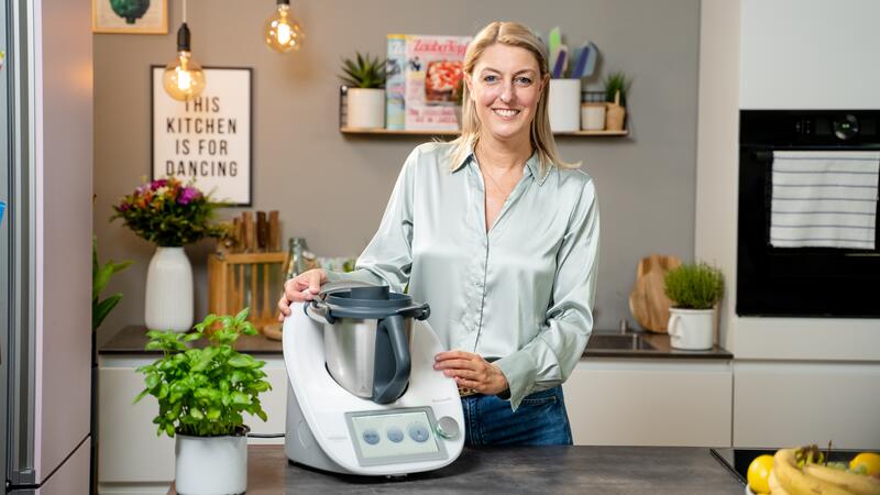 Dési steht vor dem Thermomix® und lächelt in die Kamera.