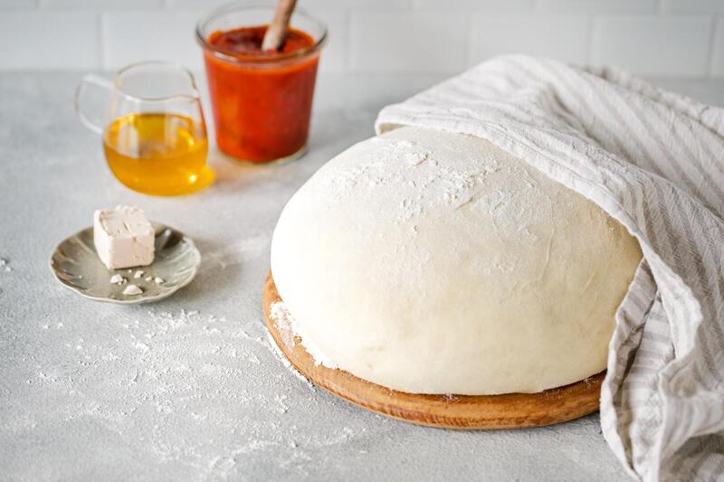 Pizzateig halb abgedeckt mit einem Küchentuch