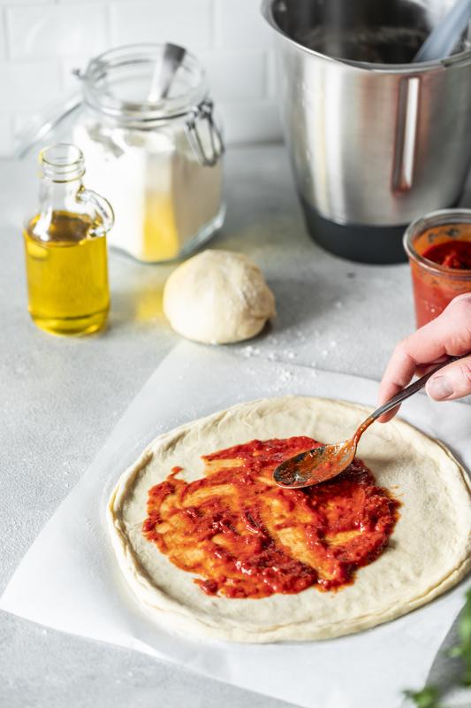 Roher Pizzateig wird mit Tomatensoße bestrichen.