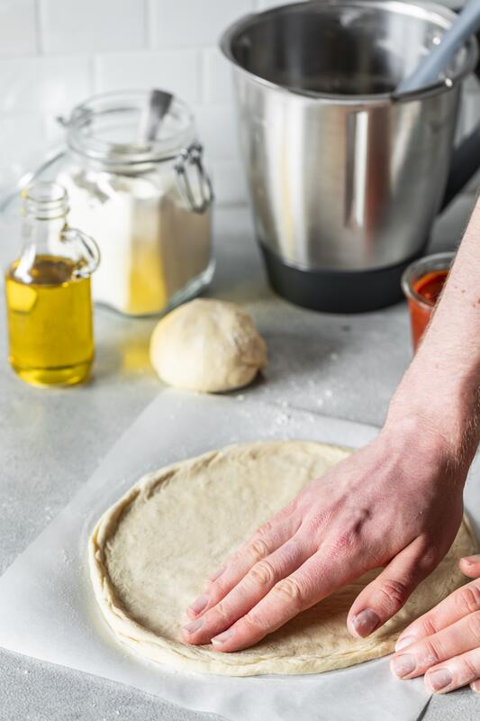 Pizzateig wird mit den Händen rund ausgerollt.