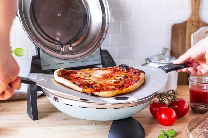 Fertige Pizza wird mit Teighebern aus dem Pizzaofen gehoben