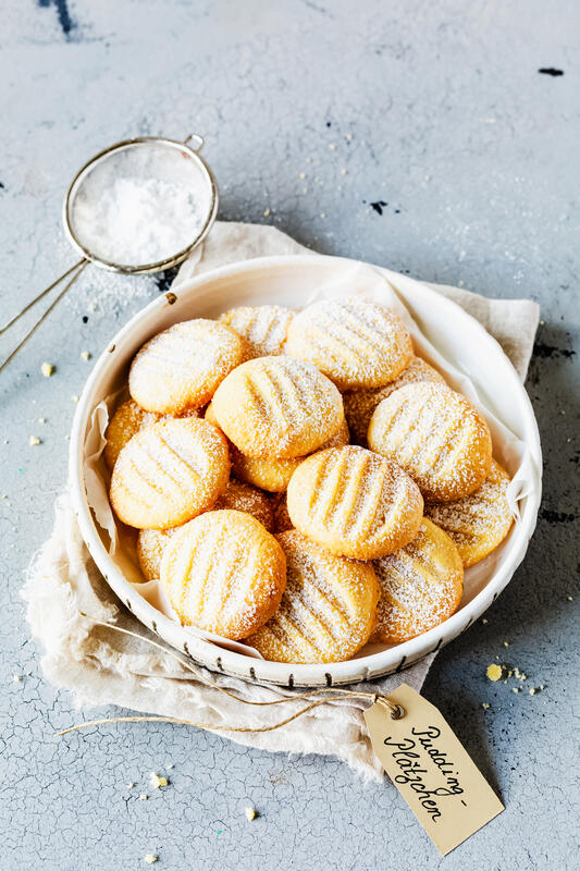 Mehrere Puddingplätzchen als Trendplätzchen mit Puderzucker bestäubt in einer Schale.