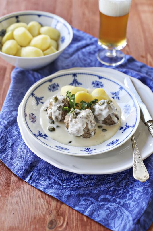 Königsberger Klopse mit Kartoffeln und Soße auf einem Teller.
