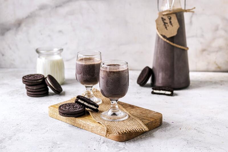 Zwei Gläser mit dunklem Likör, im Hintergrund eine Flasche, daneben Oreo-Kekse