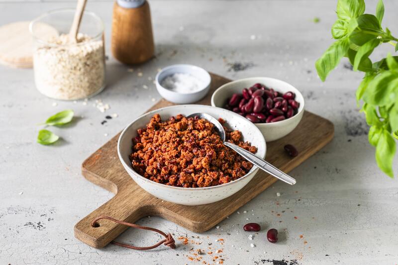 Eine Schale mit veganem Hack, dahinter eine mit Kidneybohnen, beide stehen auf einem Holzbrett