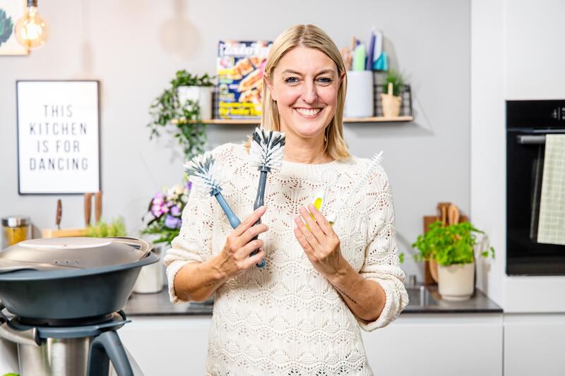 Désirée hält mehrere Bürsten für die Reinigung des Thermomix® in der Hand und lächelt