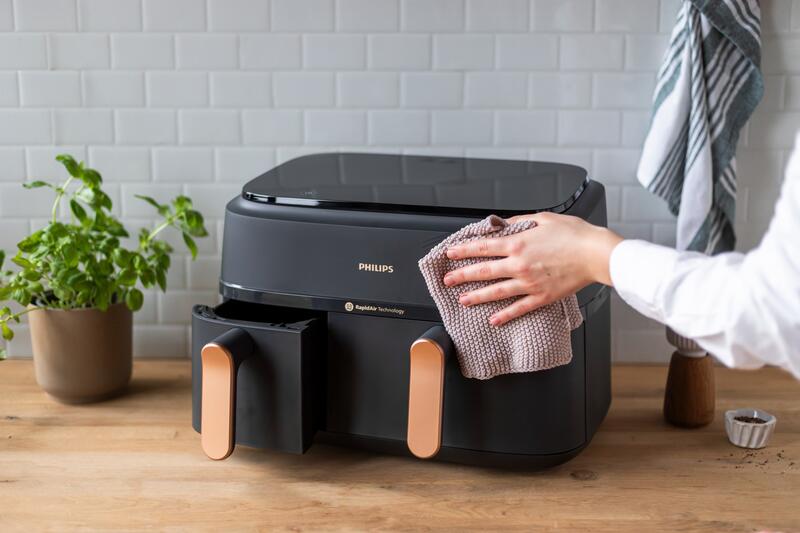 Eine Hand hält einen Lappen und wischt das Gehäuse des Airfryer ab