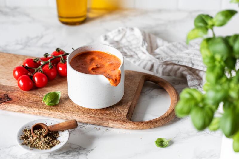 Tomatensoße in einem weißen Kännchen, daneben Tomaten