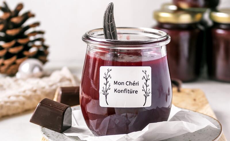 Ein Glas mit roter Konfitüre, daneben liegen Mon Chéri