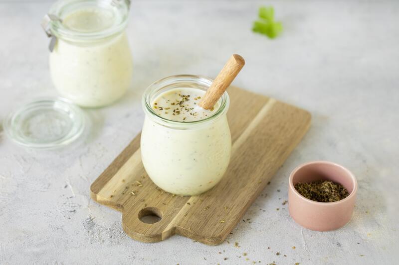 Ein Glas mit Joghurt-Salatdressing auf einem Holzbrett