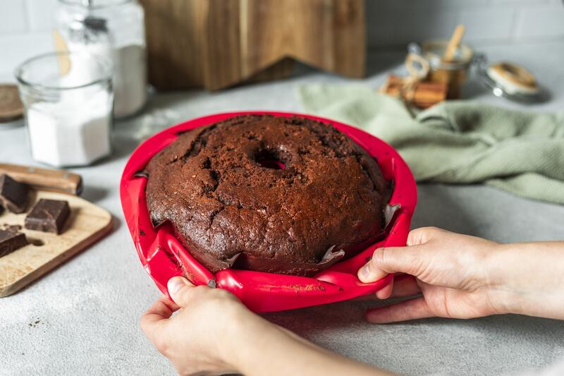 Jemand löst einen dunklen Kuchen aus einer roten Silikonform