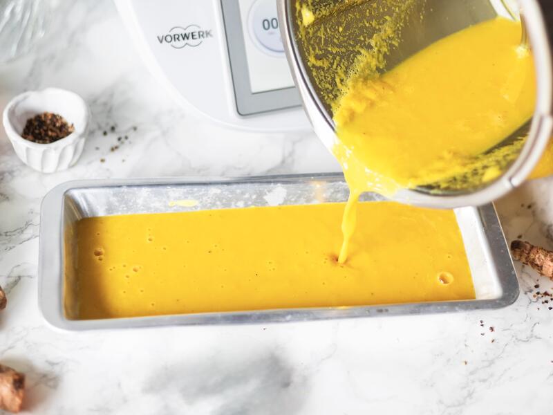 Jemand gießt Kürbissuppe aus dem Mixtopf des Thermomix® in eine flache Form