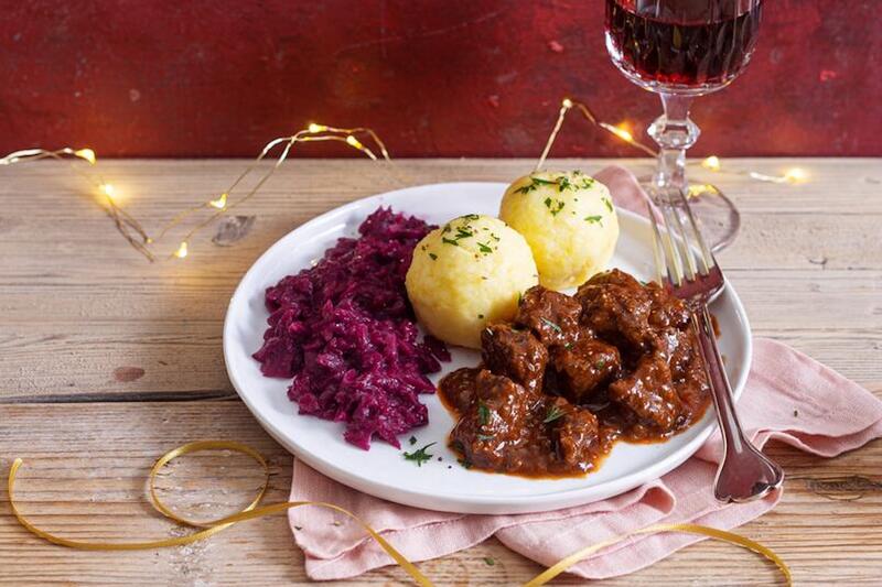 Rehgulasch mit Rotkohl und Kartoffelknödel auf einem weißen Teller