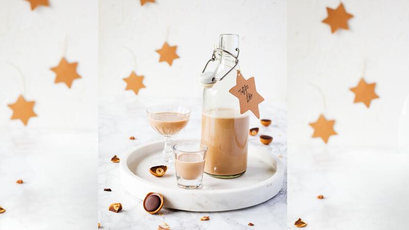 Eine Flasche mit hellbraunem Likör, daneben zwei Gläser und Toffifee