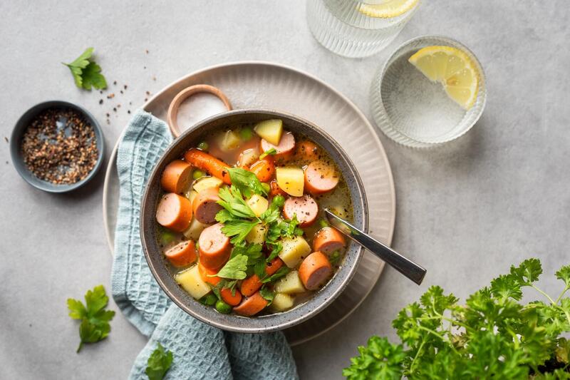 Schale mit Suppe von oben fotografiert. Darin Karotten und Würstchen