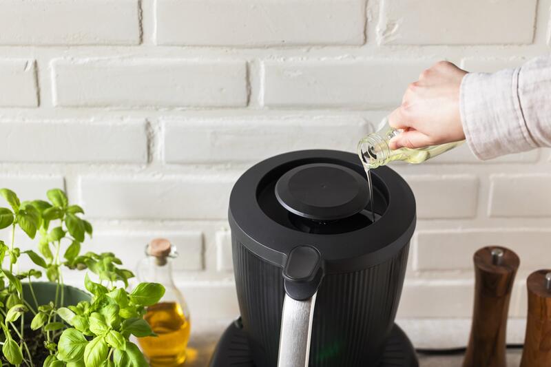 Jemand gießt Öl aus einer kleinen Flasche auf den Deckel des Thermomix®