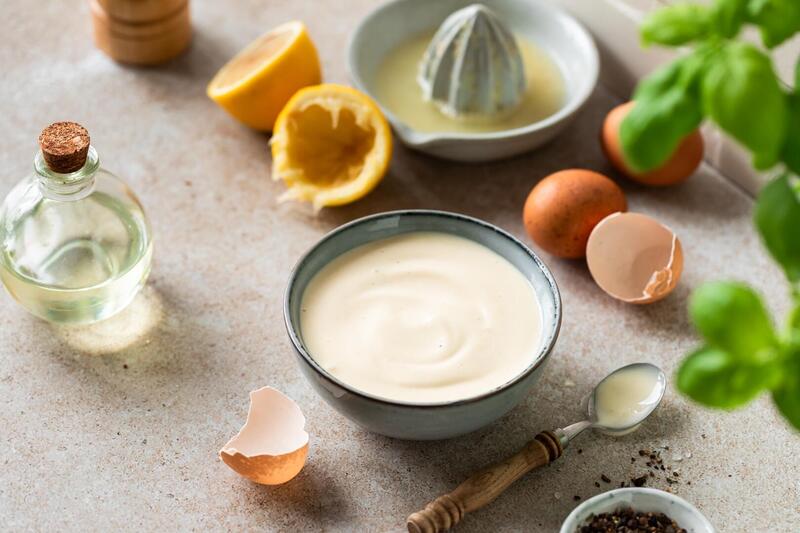 eine graue Schale mit Mayonnaise, daneben Eier, Öl, Kräuter