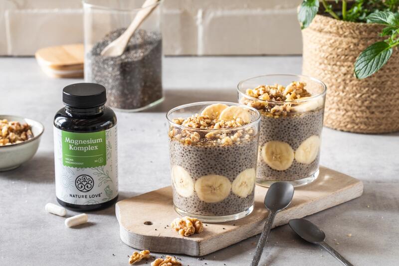 Zwei Gläser mit einem Dessert mit Chia-Samen, Banane und Walnüssen, daneben Magnesium