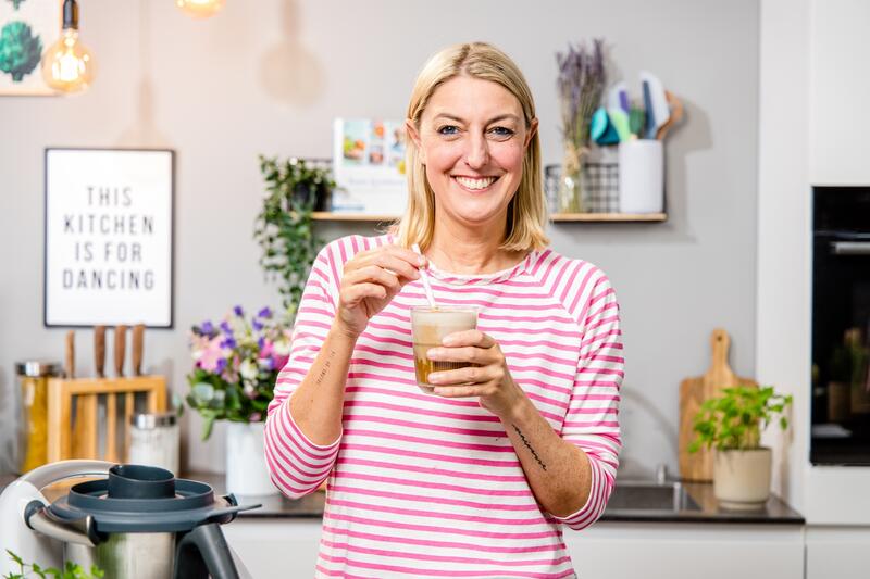 Blonde Frau in einer Küche mit einem Getränk in der Hand