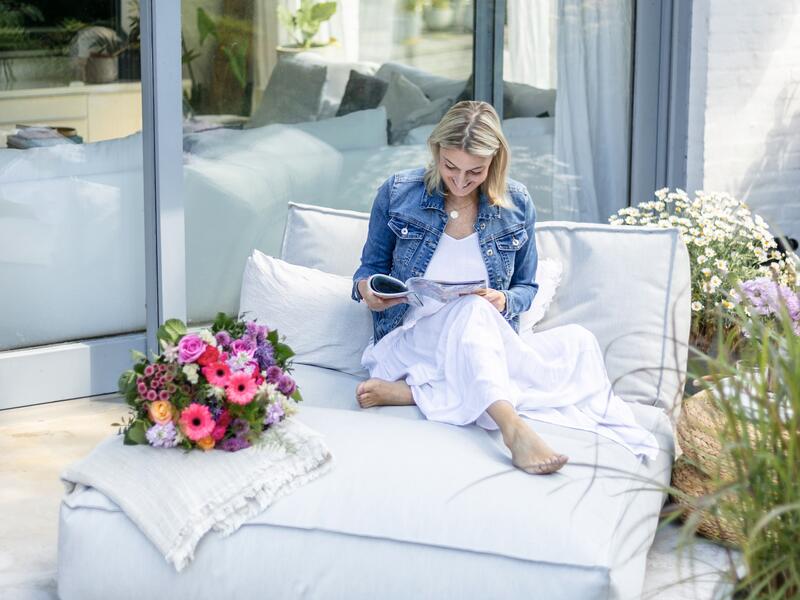 Blonde Frau in einem weißen Kleid auf einer Terrasse mit einer Zeitschrift