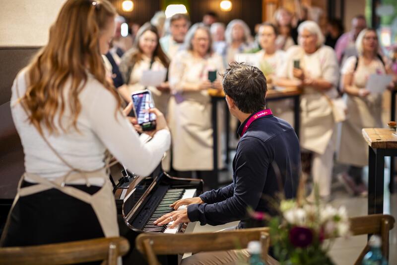 Ein Mann am Klavier im Hintergrund unscharf mehrere Menschen
