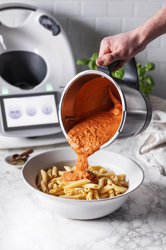 Cremige Tomatensosse wird aus dem Mixtopf auf einen Teller Nudeln gegeben