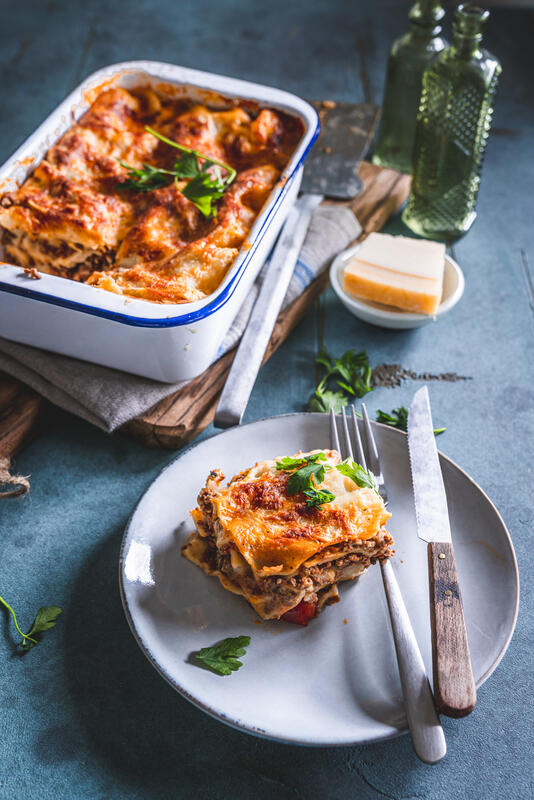 Lasagne in Auflaufform und ein Stück auf einem Teller mit Petersilie.
