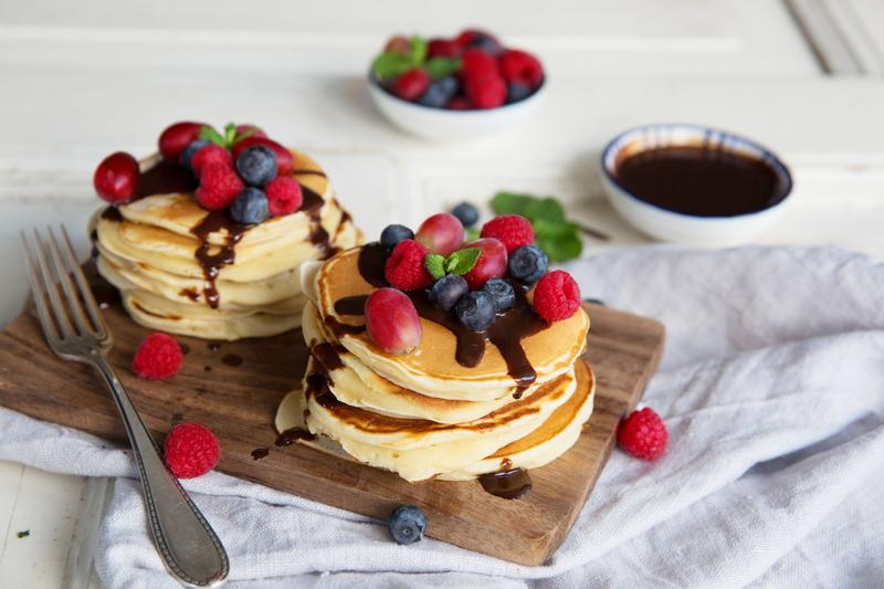 Pancakes mit Obst und Schokosoße auf Holzbrett 