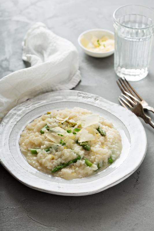 Risotto mit grünem Spargel in tiefem, weißen Teller mit Parmesanhobeln garniert