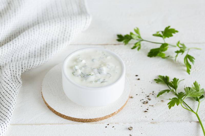 Joghurt-Dip in kleiner weißer Schale mit angelegten Kräuterstielen
