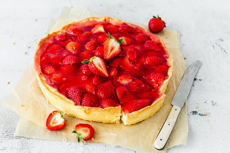 Erdbeerkuchen in Herzform auf weißem Untergrund mit angestellten Erdbeeren