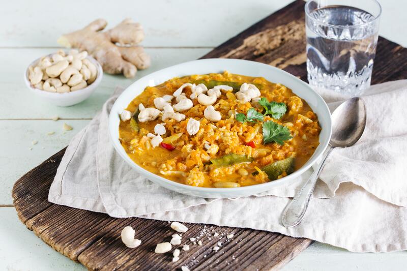 Weißer Teller mit Blumenkohlcurry mit angelegtem Löffel, Glas und Cashews