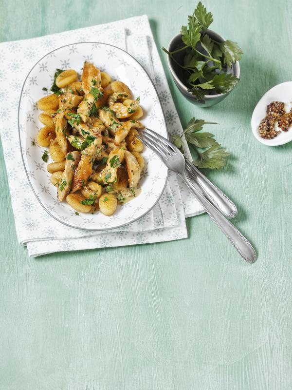 Ein Teller mit Gnocchi und Hähnchen mit Petersilie und Sauce garniert.