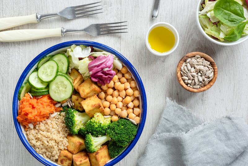 Blaue Schale mit Kichererbsen, Tofu, Brokkoli, Quinoa, Karotte, Gurke und Olivenöl & Sonnenblumenkernen im Schälchen