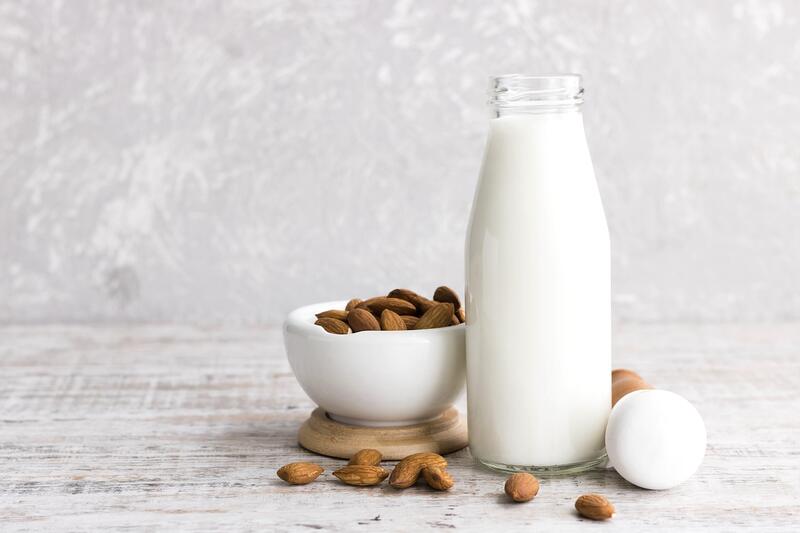 Große Flasche mit Mandelmilch aus dem Thermomix® mit angestellten Mandeln in kleiner Schale