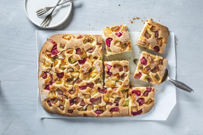 Angeschnittener Rhabarberkuchen mit Apfel vom Blech von oben fotografiert auf hellgrauem Untergrund