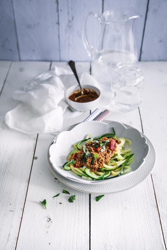 Tiefer weißer Teller mit Zucchini-Nudeln und Bolognese auf weißem Holzuntergrund