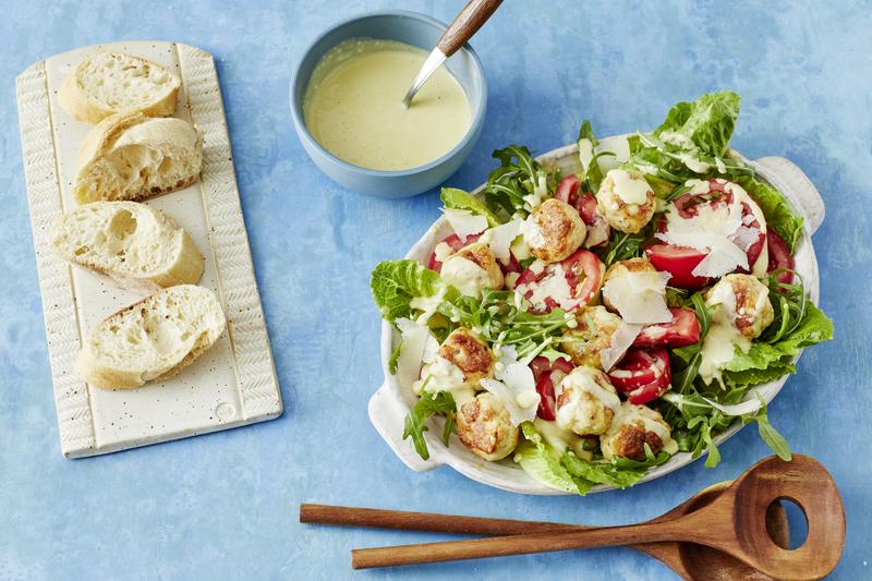 Weiße ovale Schüssel mit Caesar Salad mit dem Thermomix® auf blauem Untergrund