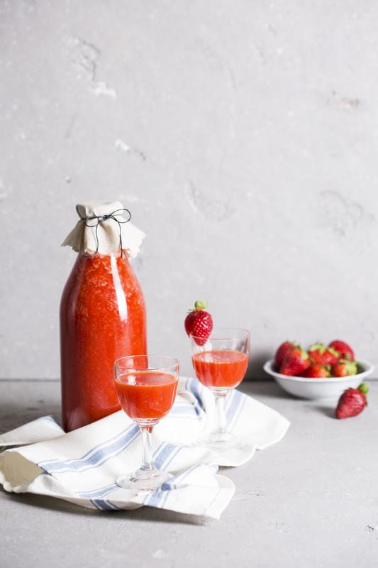 Große Flasche mit Erdbeerlimes aus dem Thermomix® mit zwei Schnapsgläschen und Schälchen mit Erdbeeren