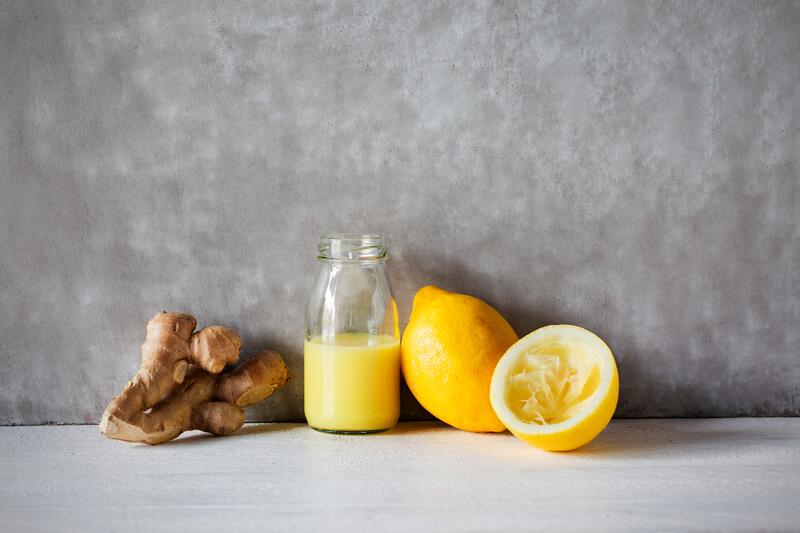 Ingwer-Zitrone-Shot in einer Glasflasche, daneben Zitronen und Ingwerknollen