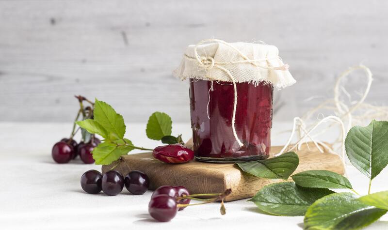 Marmeladenglas auf Holzbrett mit Kirschmarmelade aus dem Thermomix® mit angelegten Kirschen