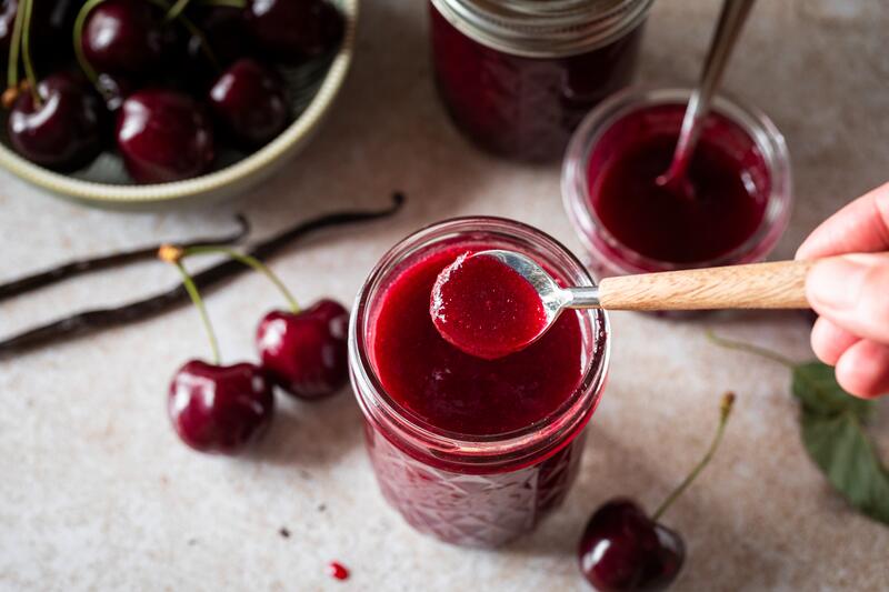 Marmeladenglas auf Holzbrett mit Kirschmarmelade aus dem Thermomix® mit angelegten Kirschen