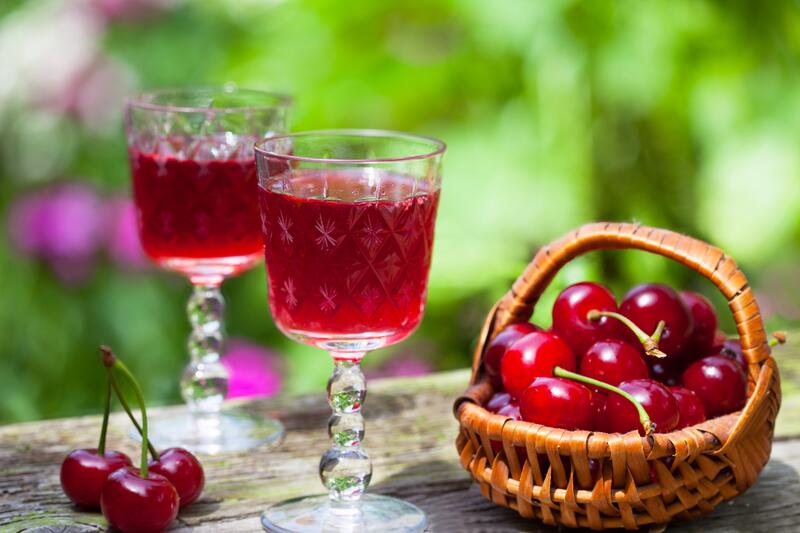Zwei Gläser mit Kirschlikör mit angestelltem Körbchen mit Kirschen auf Tisch mit Garten im Hintergrund