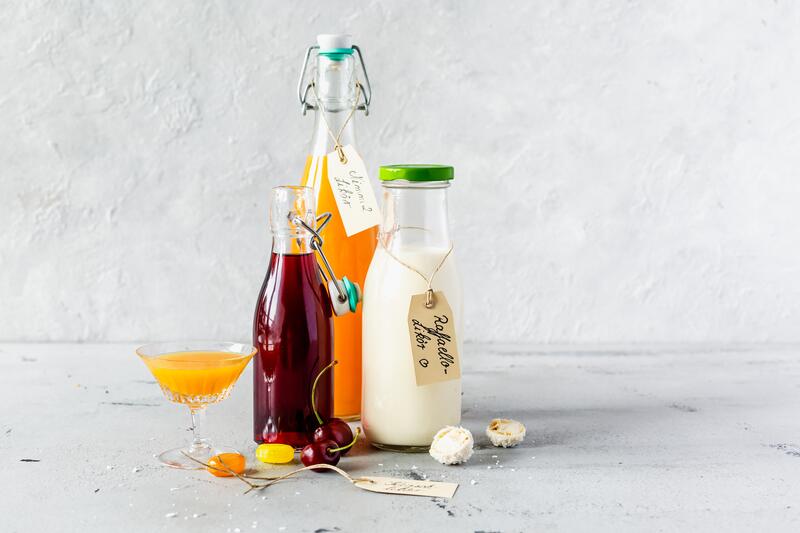 Zwei Gläser mit Kirschlikör mit angestelltem Körbchen mit Kirschen auf Tisch mit Garten im Hintergrund